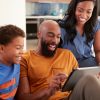 African American Family With Son Sitting On Sofa At Home Using Digital Tablet