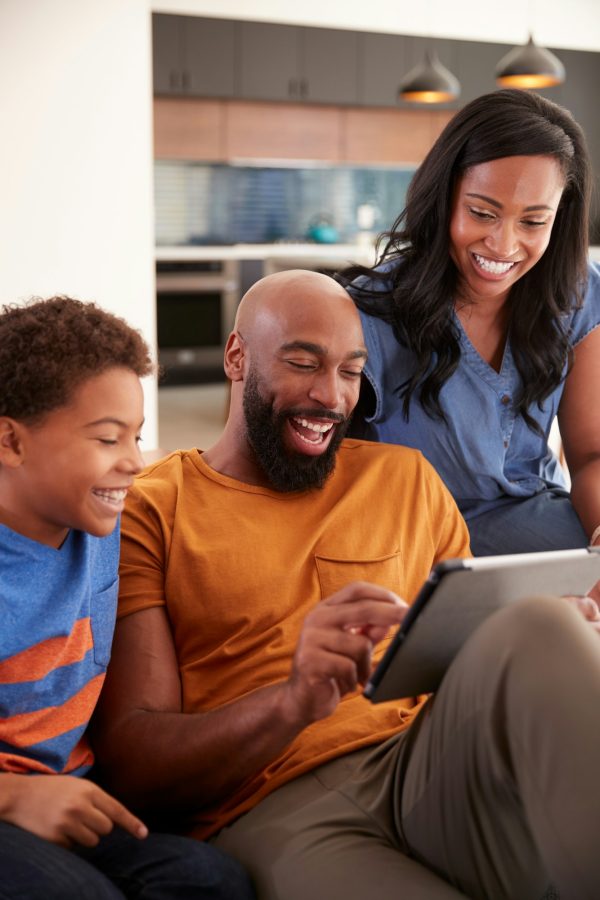 African American Family With Son Sitting On Sofa At Home Using Digital Tablet