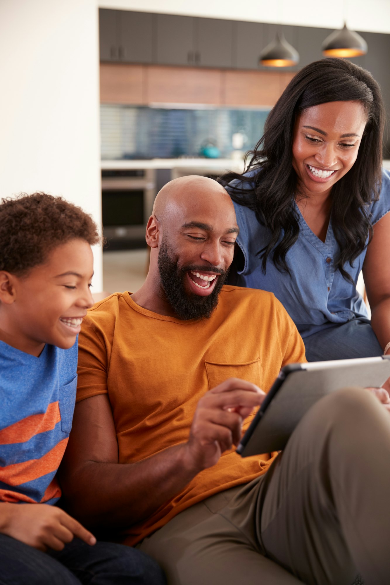 African American Family With Son Sitting On Sofa At Home Using Digital Tablet